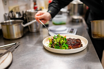 professional chef's hands cooking Grilled Ribeye Steak on plate with Potato gratin and salad in