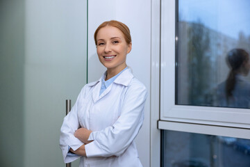 Blonde young female doctor standing in hospital near widow , working in nursing home.