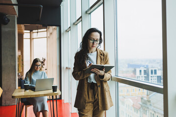A successful woman in glasses works in the office on the background of colleagues. Modern working day in the office. Businesswoman makes notes in a notebook