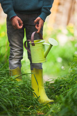 Legs of a child wearing wellies and holding a watering can. © OR MIXphoto