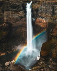 The landscape of Haifoss waterfall with a vivid rainbow arching above it.