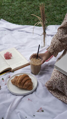 girl picnic hold a coffee milk and croissant butter while reading book