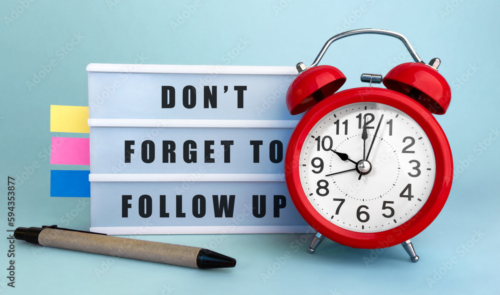 Poster text dont forget to follow up written on the lightbox with alarm clock and colorfull stickers on blu