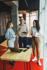 Modern pregnant woman working in office with colleagues. A young successful man helps a pregnant colleague at work. A beautiful pregnant woman works in the office. Modern pregnant woman