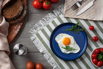 Fried eggs for breakfast. Healthy breakfast with vegetables and herbs. Fried egg on a blue plate. Serving on the table 
