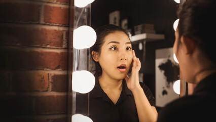 Asian woman shocked Reflection in the mirror. Woman looks in the mirror noticing the first wrinklesaction on mirror with eyes wrinkle on face and need skin care