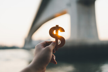 Businessman's hand holding a symbol Dollar with blur bridge construction background, concept of real estate investment.