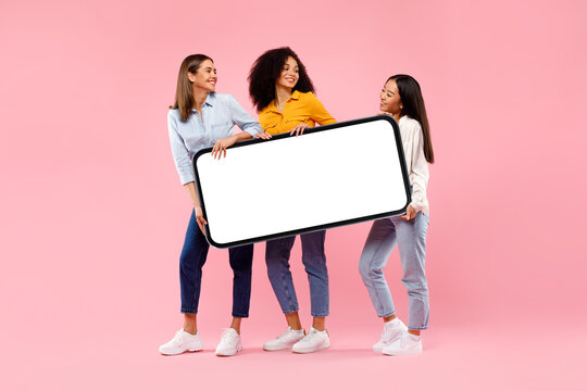 Young Diverse Women Holding Giant Smartphone With Mockup For Ad, Demonstrating Space For Your Design, Full Length