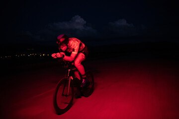 Fototapeta na wymiar A triathlete rides his bike in the darkness of night, pushing himself to prepare for a marathon. The contrast between the darkness and the light of his bike creates a sense of drama and highlights the