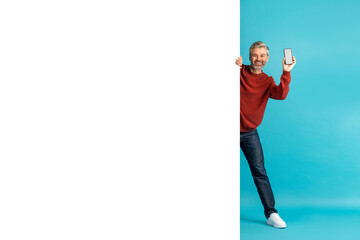 Excited middle aged man with smartphone standing by advertising board