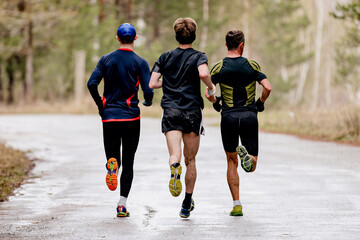 rear view three male runners running spring running on road in with puddles, splashes water and dirt on feet