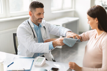 Obraz premium Middle aged male doctor gynecologist checking young pregnant lady heart rate and blood pressure, using tonometer