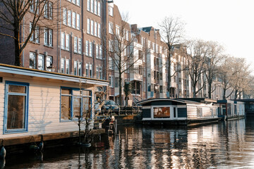 Fototapeta na wymiar Aesthetic canals of Amsterdam at sunset, view from the water, houseboats on the canal, houseboats hotels. Romantic canal boat ride in Amsterdam.