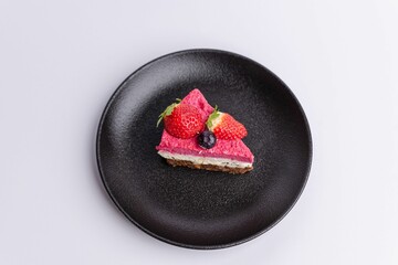 Delicious slice of strawberry-topped cheesecake on a matte dark grey plate on a white background