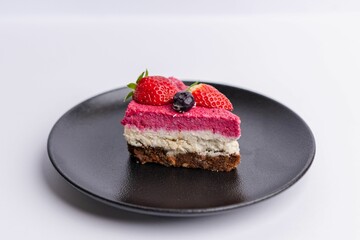 Delicious slice of strawberry-topped cheesecake on a matte dark grey plate on a white background