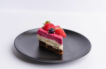 Delicious slice of strawberry-topped cheesecake on a matte dark grey plate on a white background