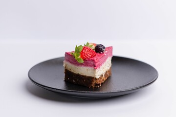 Delicious slice of strawberry-topped cheesecake on a matte dark grey plate on a white background