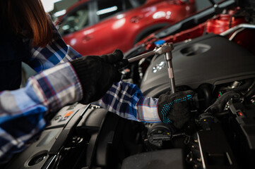 Female auto mechanic unscrewing a nut to replace a car spark plug.