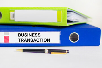 BUSINESS TRANSACTION text on a folder with documents with a pen on a white background
