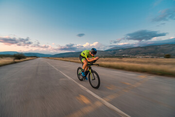  Triathlete riding his bicycle during sunset, preparing for a marathon. The warm colors of the sky provide a beautiful backdrop for his determined and focused effort.