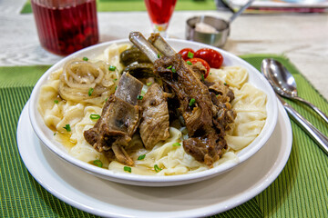 Beshbarmak dish: noodles with lamb and onion close-up on a plate on the table. Large pieces of stewed meat are cooked on plates test