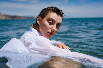 beautiful girl with a short haircut in a white shirt bathes in the sea. fashion shooting