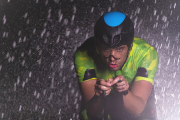 A triathlete braving the rain as he cycles through the night, preparing himself for the upcoming marathon. The blurred raindrops in the foreground and the dark, moody atmosphere in the background add