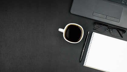 Desk workspace. Blank notepad, pen, glasses, laptop and coffee on dark table. 