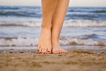 
Photo of Female Feet Together with Red Painted Toenails Leaving the Sea with Water Drops on the Sand. Concept of caring for the health of the feet