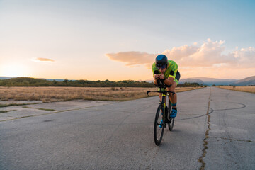  Triathlete riding his bicycle during sunset, preparing for a marathon. The warm colors of the sky...