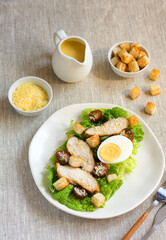 Caesar salad with croutons, fried chicken, cherry tomatoes, egg and parmesan cheese on a light plate with a fork, on a linen tablecloth in a plate of grated parmesan cheese and cherry tomatoes