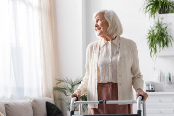 happy senior woman with grey hair walking with help of walker at home.