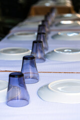 Table in empty restaurant with white plates and blue glasses.