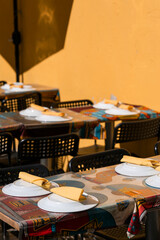 Empty outdoor restaurant with tables set for food with dishes and tablecloth on sunny day.