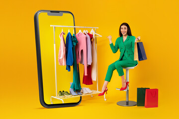 Excited caucasian shopaholic woman pointing at clothing rail in giant cellphone, choosing and...