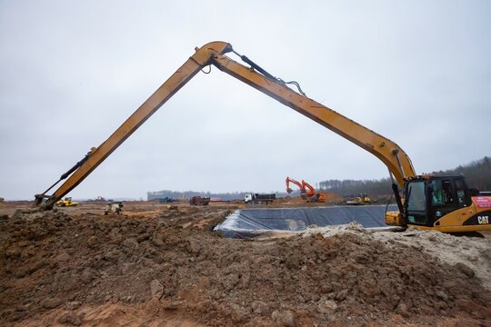 Ust-Luga, Leningrad oblast, Russia - November 16, 2021: Ground works and chemical waste ditch creation. Caterpillar excavator with long boom flatten ground