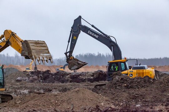 Ust-Luga, Leningrad oblast, Russia - November 16, 2021: John Deere excavators digging ditch in rainy day.
