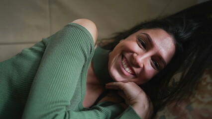 Obraz premium One joyful young woman smiling and laughing while laying on couch. Closeup face of adult girl in 20s feeling happiness