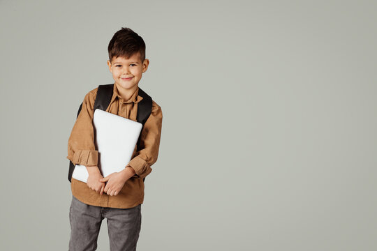 Happy little european child 6 years old pupil in casual with backpack and laptop