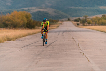 Fototapeta premium Triathlete riding his bicycle during sunset, preparing for a marathon. The warm colors of the sky provide a beautiful backdrop for his determined and focused effort.