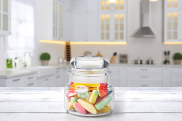 Glass jar with tasty gummy candies on white wooden table in kitchen