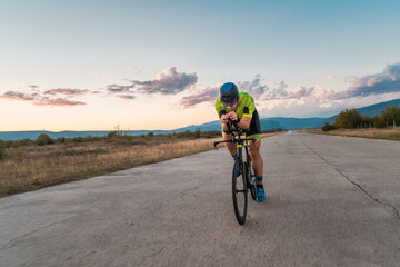 Fototapeta premium Triathlete riding his bicycle during sunset, preparing for a marathon. The warm colors of the sky provide a beautiful backdrop for his determined and focused effort.