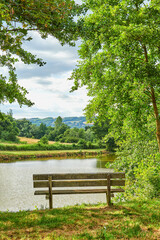 Fototapeta na wymiar A bench overlooking a lake in the countryside, surrounded by farmland and a forest close to Lyon, France. A quiet place to relax and reflect. Find some peace and tranquility outside in nature