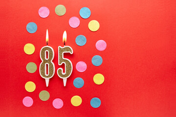 Number 85 on a red background with colored confetti. Happy birthday candles. The concept of celebrating a birthday, anniversary, important date, holiday. Copy space. banner
