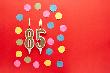 Number 85 on a red background with colored confetti. Happy birthday candles. The concept of...