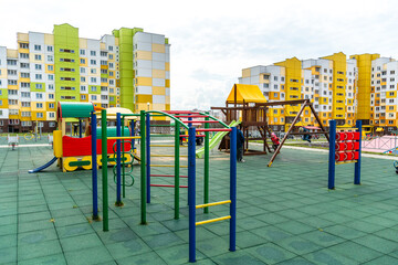 Fototapeta na wymiar A modern outdoor playground in the courtyard of a building. Colorful children's swings and slides for recreation and games are installed. Playground on the background of residential buildings.