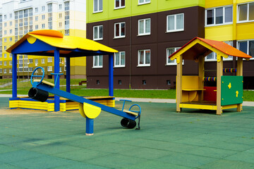 A modern outdoor playground in the courtyard of a building. Colorful children's swings and slides for recreation and games are installed. Playground on the background of residential buildings.