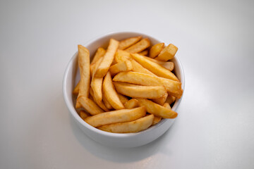 French fries serve in white bowl on white table.