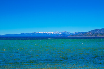 View of Lake Tahoe from Shore looking towards Mt. Rose and Incline Village, with a a saliboat mid frame - obrazy, fototapety, plakaty