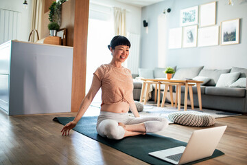 Young Japanese woman doing yoga while using a laptop